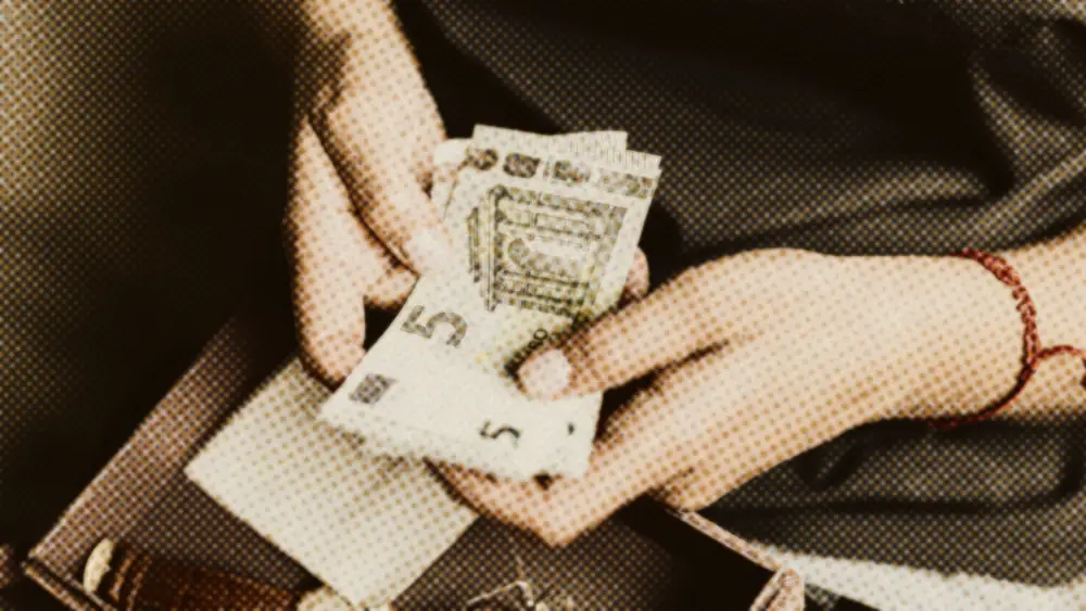 Two hands holding a five-euro banknote taken from a small keepsake box, weighing an everyday money decision