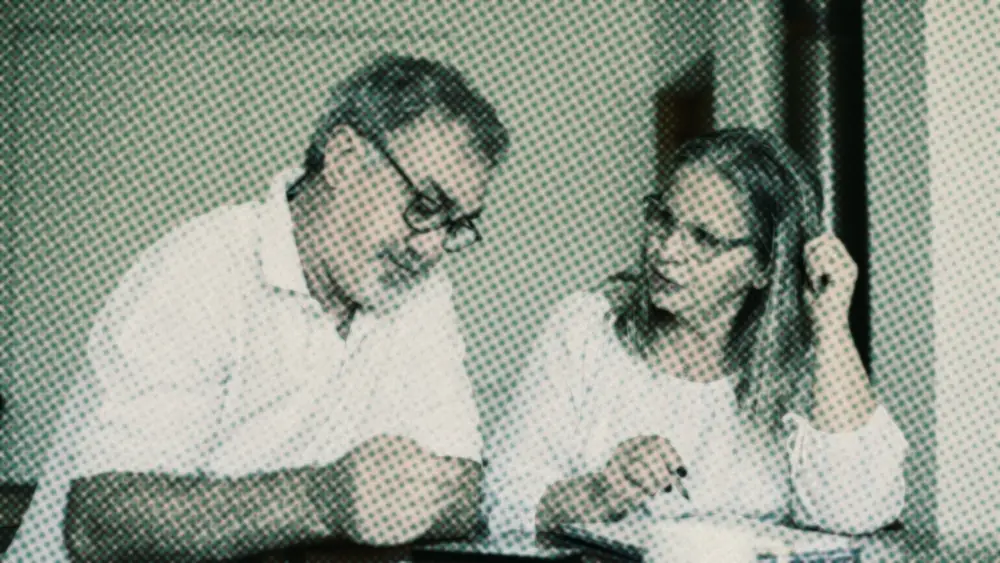 Older couple in glasses going over financial paperwork at a wooden table with a coffee cup