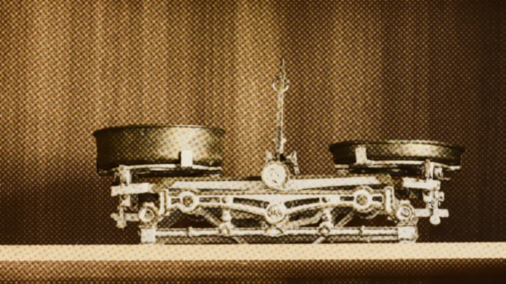 Brass two-pan balance scale on a wooden shelf, one pan tipped lower than the other.