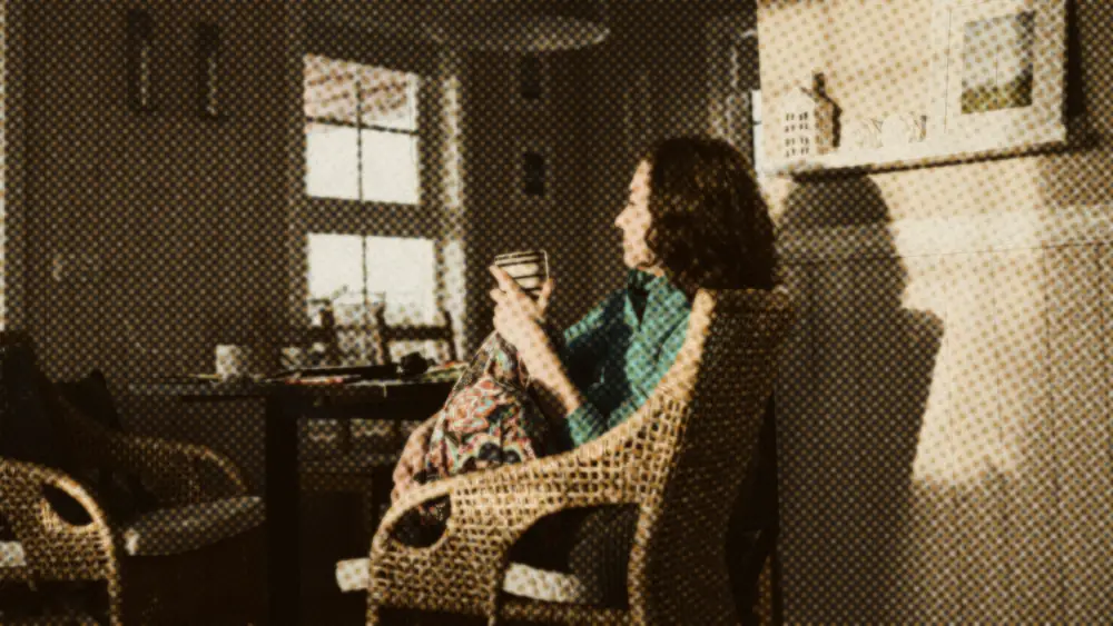 A woman sits back in a wicker chair with a mug, gazing into warm afternoon light in a calm home interior