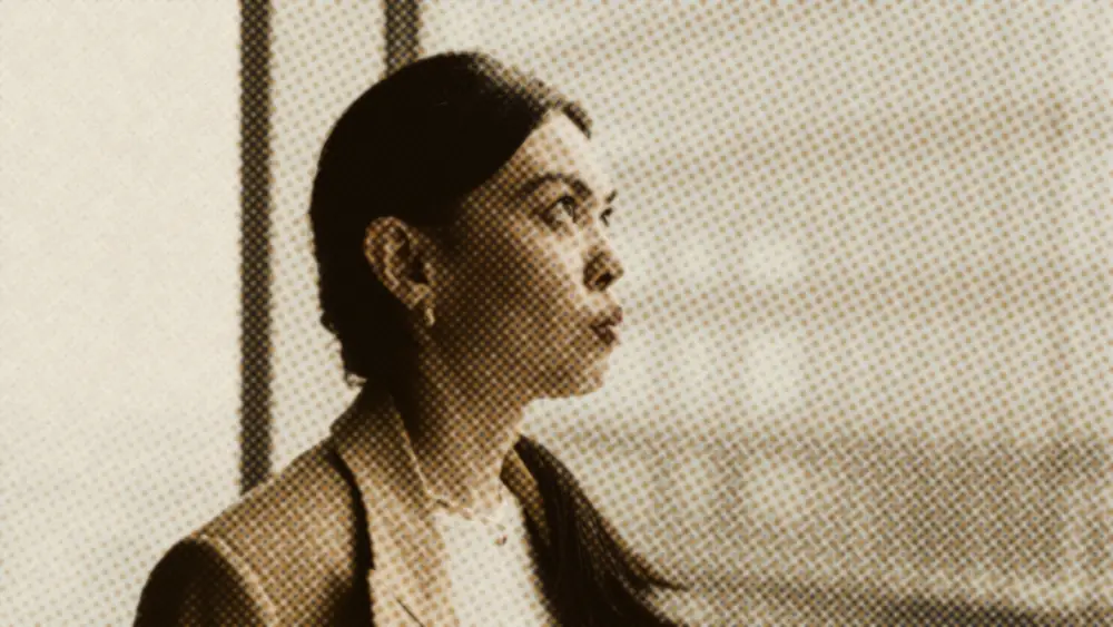 A professional in a blazer gazes thoughtfully out of a high office window over a glass city building