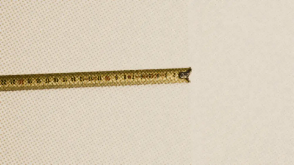 A metal tape measure extended across a plain pale wall, its printed numbers running along the edge