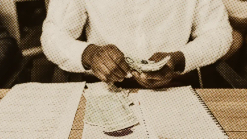 Person at a desk counting 100-euro banknotes beside a handwritten budget notebook and household papers