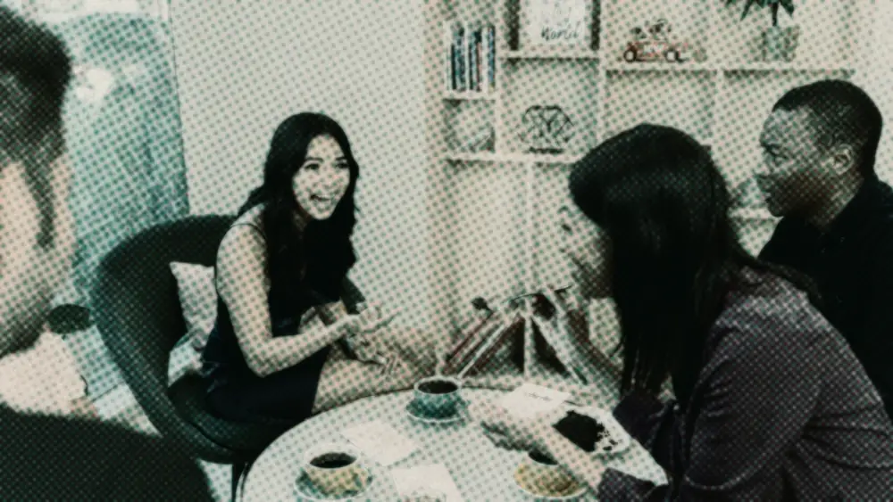 A diverse group of four friends talking and laughing over coffee and cake at a cafe table