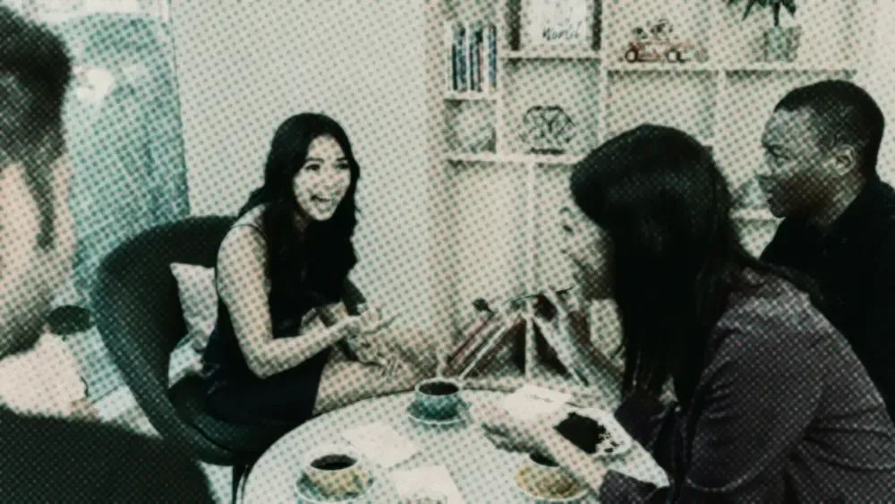 A diverse group of four friends talking and laughing over coffee and cake at a cafe table