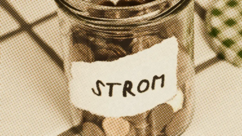 A glass jar of copper euro-cent coins on a tiled table, hand-labelled STROM, the German for electricity