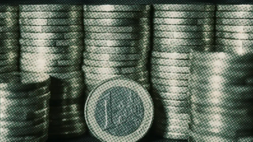 A single one-euro coin standing upright in front of tall, even rows of stacked euro coins
