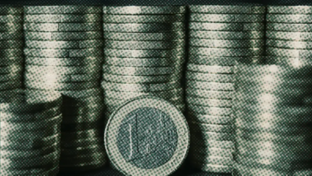 A single one-euro coin standing upright in front of tall, even rows of stacked euro coins