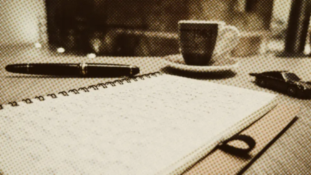 Handwritten notes fill a spiral notebook beside a fountain pen and an espresso cup on a wooden table