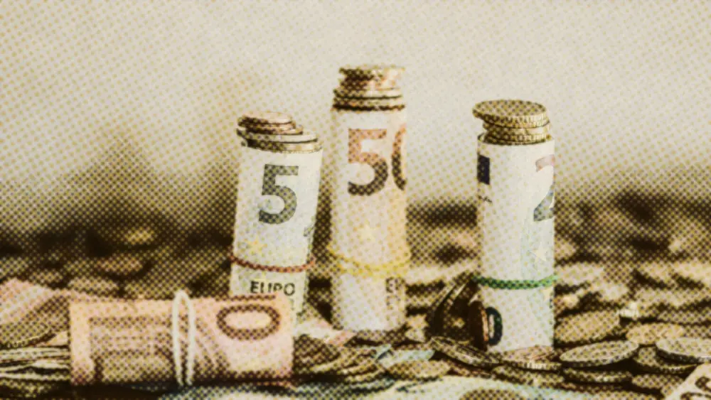 Three rolled euro banknotes standing on a thick bed of euro coins and loose notes