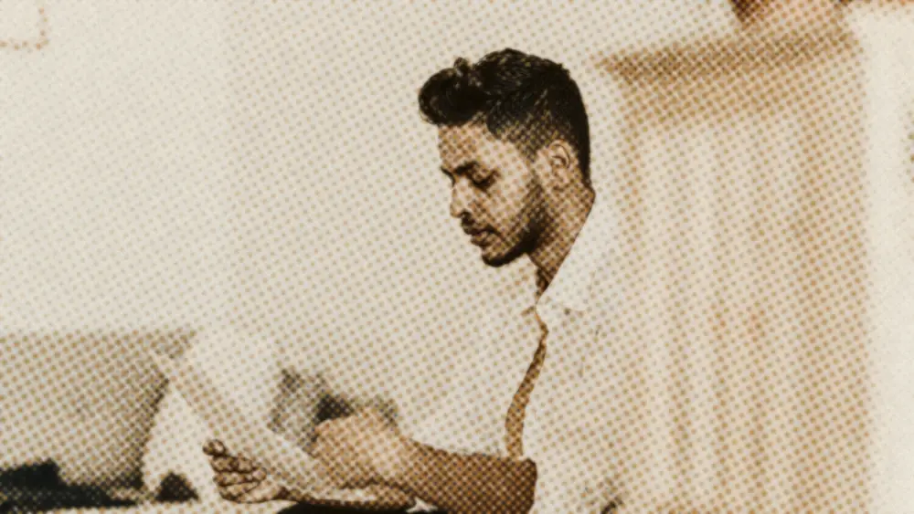 Man calmly reading a printed paper document, seated in a bright, naturally lit room