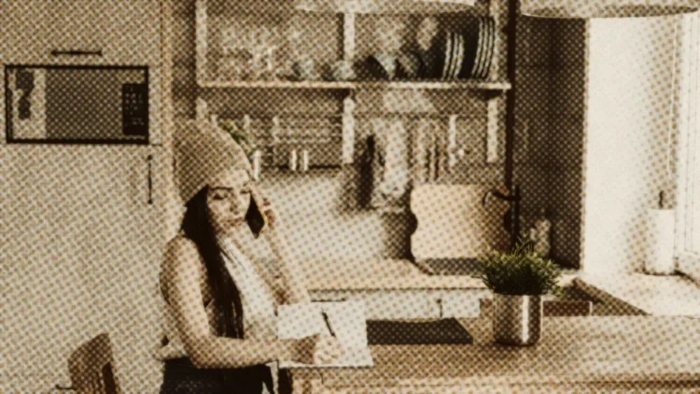 Calm young woman on the phone taking notes at a kitchen table in a bright modern home