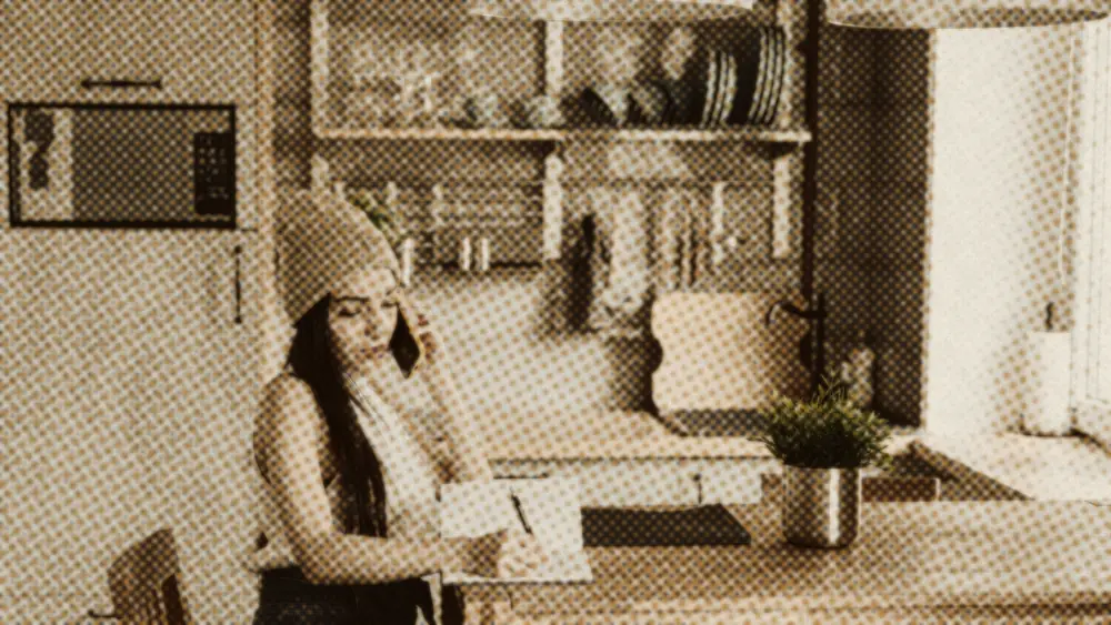 Calm young woman on the phone taking notes at a kitchen table in a bright modern home