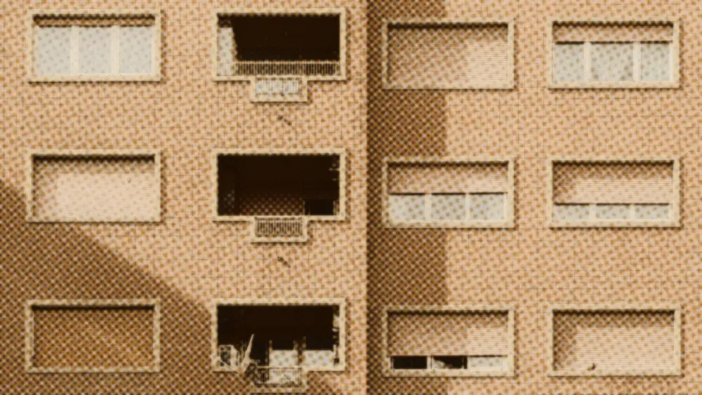 Rows of windows and closed roller shutters on the plain brick facade of an ordinary apartment block